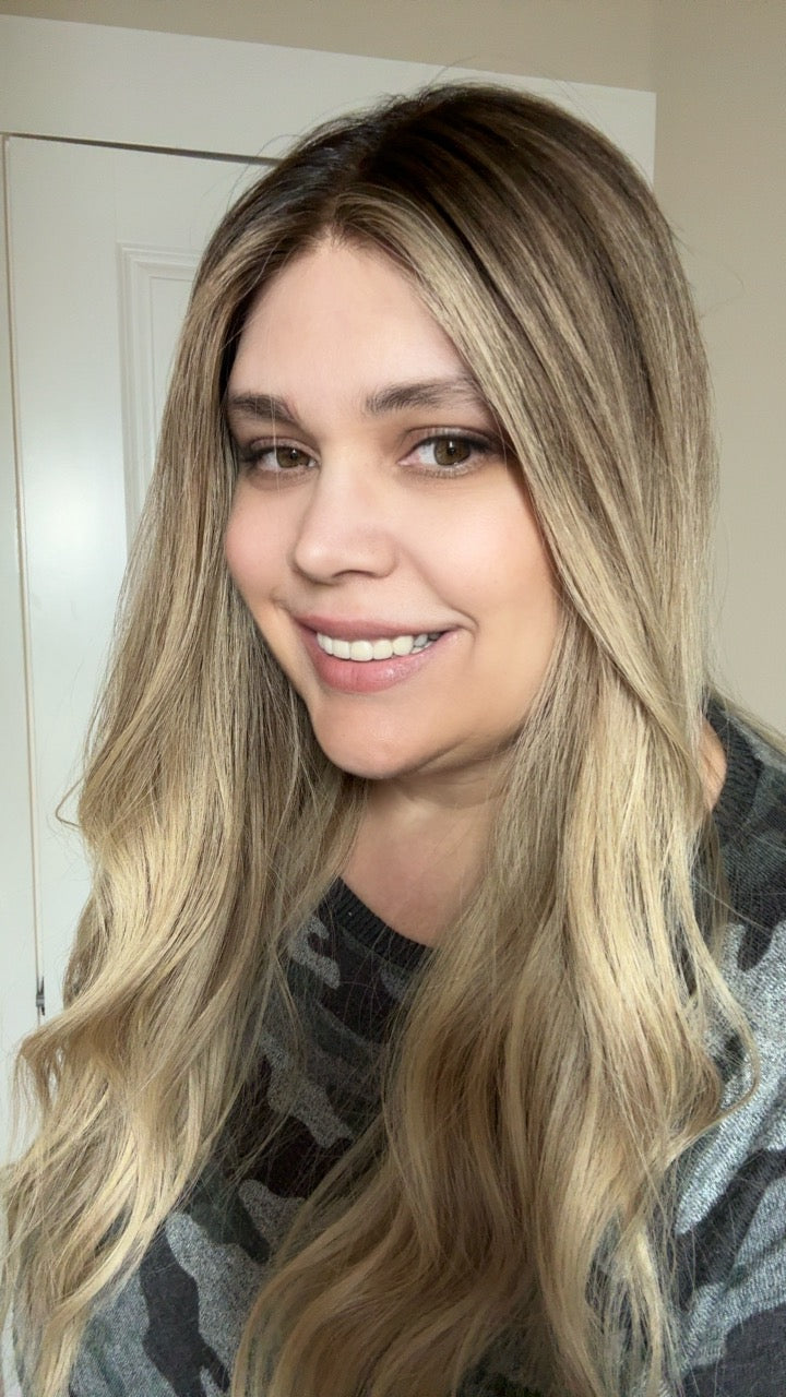 Woman with long blonde hair smiling in front of a white door.
